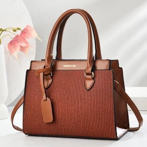 Détail de la texture plissée rouge rouille et lettrage doré sur sac à main chic