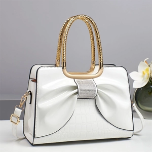 Detail of white handbag with large crystal bow, crocodile texture and golden handle