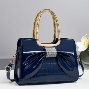 Detail of dark blue patent leather handbag with rhinestone bow and gold handle