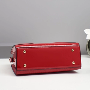 Detail view of red crocodile-embossed patent leather bag with gold protective metal feet