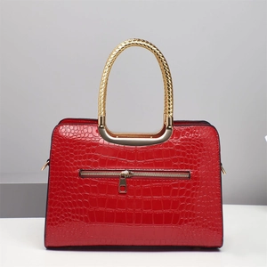 Detail of red crocodile texture handbag with gold braided handle and outer zipper pocket