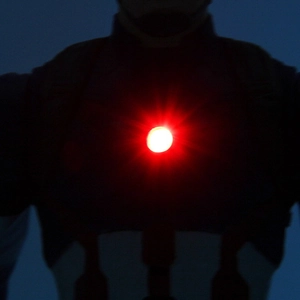 Macro shot of wearable red LED light glowing on tactical chest gear for night safety