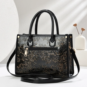 Close-up of black embossed floral pattern on glossy handbag with golden hardware