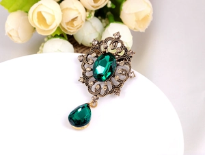 Close-up of vintage bronze brooch with sparkling green gemstone and rhinestone accents