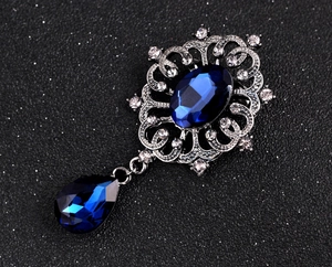 Detailed close-up of vintage brooch with blue gemstone and rhinestones on dark background