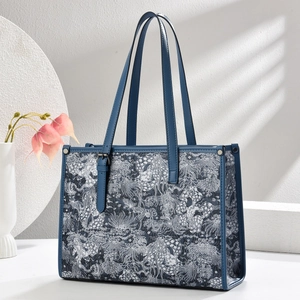 Detail of blue tote bag with white floral embroidery and sturdy leather handles