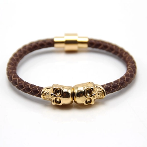 Macro detail of men's brown leather braided bracelet with gold skull charms and clasp