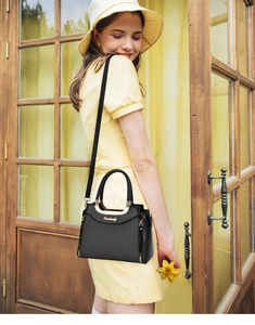 Outdoor shot of a black woven pattern tote bag with gold hardware and shoulder strap