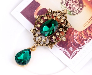 Detailed view of vintage bronze leaf brooch with emerald green crystals and rhinestones