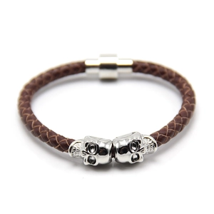 Close-up of brown braided leather bracelet featuring silver skull charms and magnetic clasp