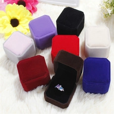 Various colorful velvet ring boxes stacked on white faux fur with floral accents