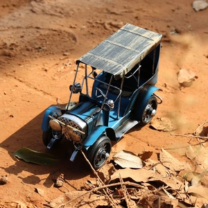 Détail d'un modèle de voiture rétro en métal bleu sur un fond de terre sablonneuse