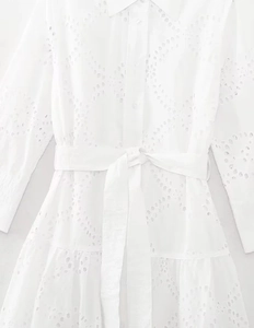 Close-up of white eyelet embroidery fabric on a long sleeve dress with waist belt