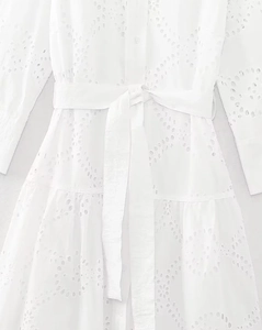 Detailed view of white embroidered hollow-out fabric with a matching waist belt bow