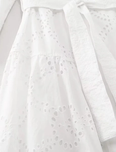 Detail showing white eyelet embroidery patterns and cotton waist tie on the dress