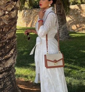 Close-up of white lace dress with intricate embroidery and a tan crossbody bag