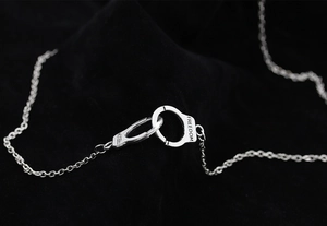 Detailed close-up of interlocking silver handcuffs necklace engraved with freedom text