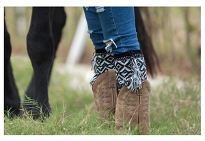 Detail of bohemian knit leg warmers with geometric patterns and tassels over brown boots