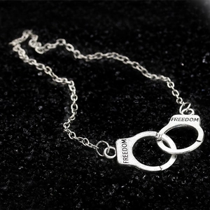 Close-up of silver handcuff charm engraved with FREEDOM on a black stone background