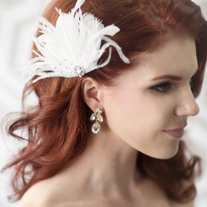 Detail of elegant white feather fascinator and teardrop crystal earrings on a bride