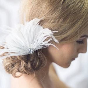 Detail of white bridal feather headpiece with sparkling rhinestone center on elegant hairstyle