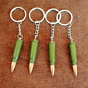 Detail of four green and bronze metal bullet shell keychains on textured fabric