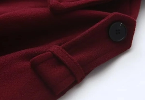 Macro view of burgundy wool coat showing sleeve tab and matte black four-hole button