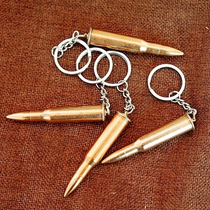 Close-up of four bronze-tone metal bullet-shaped keychains on woven fabric background