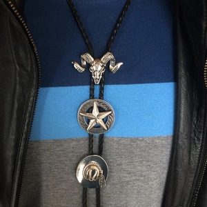 Detail of vintage silver bull skull star and cowboy hat bolo tie pendants on woven cord