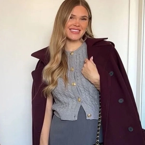 Detail of burgundy wool coat paired with grey cable knit vest and gold embossed buttons