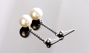 Close-up of elegant long tassel pearl earrings with silver finish on dark mirror