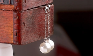 Close-up of long silver pearl tassel earrings draped over a vintage wooden box