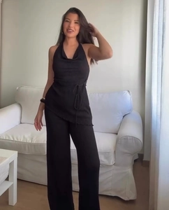 Dettaglio del top nero plissettato con scollo a drappeggio e pantaloni a gamba larga