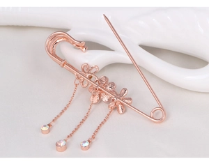 Close-up of rose gold safety pin brooch with flower charms and rhinestone tassels