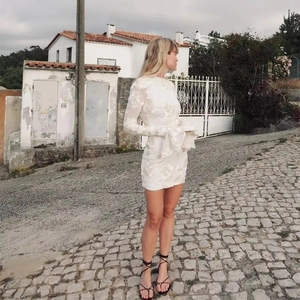 Détail de la robe moulante blanche avec broderie florale 3D et manches cloches à volants