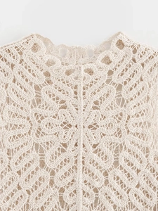 Detailed close-up of intricate crochet patterns on cream sleeveless knit top