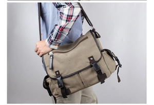 Close-up of a khaki canvas messenger bag with brown leather trim worn by a model