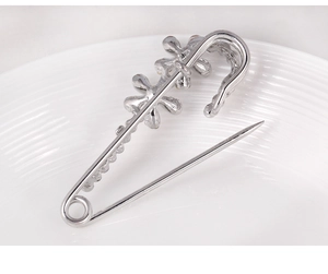 Close-up of silver safety pin brooch with sparkling floral crystals on a white ceramic plate