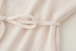Dettaglio del tessuto testurizzato crema con cintura a nodo regolabile sui pantaloni