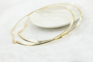 Polished gold rigid choker necklace with adjustable chain on white plush background