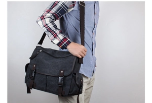 Detail view of large dark grey canvas messenger bag with leather trim on model