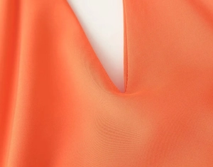 Close-up detail of the orange V-neck strap dress showing soft fabric texture and stitching