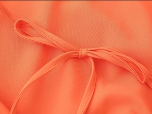 Detailed macro view of vibrant orange woven dress showing intricate strap bow craftsmanship