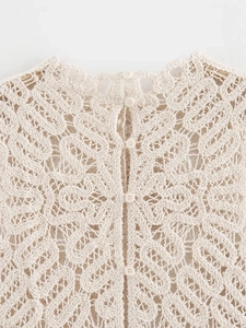 Close-up of beige crochet knit top showing intricate hollow patterns and small round buttons