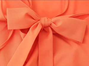 Detail shot of coral orange dress featuring a delicate bow tie and smooth fabric texture