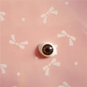 Detailed view of 10x14mm brown acrylic doll eyes with intricate iris texture on pink card