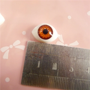 Detailed view of a 12x16mm brown acrylic doll eye measured with a metal ruler