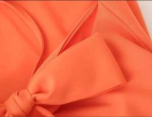 Close-up of bright orange dress featuring a structured bow detail and fine fabric texture
