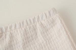 Dettaglio dell'elastico in vita su pantaloni bianchi plissettati in tessuto stropicciato