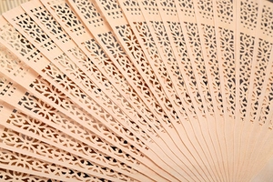Detail view of intricately carved hollow patterns on the natural sandalwood folding fan